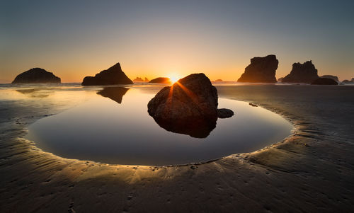 Rocks on sea shore against sky during sunset