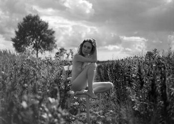 Portrait of naked woman sitting on bench at field against sky