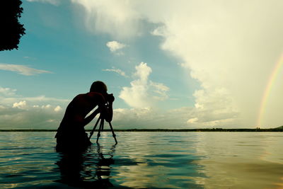 Man photographing with camera in lake against sky during sunset