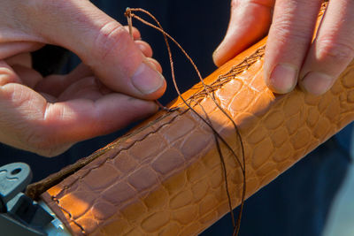 Cropped hands of man stitching leather on metal