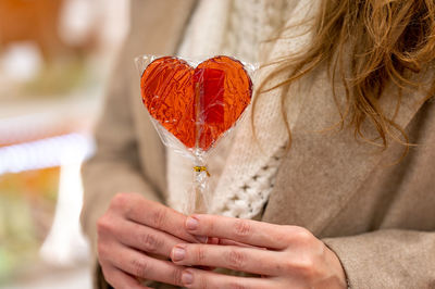 Girl holding a heart-shaped lollipop in her hands. the girl's face is not visible. valentine's day