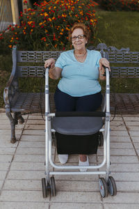 Smiling senior woman in front of walker sitting on bench
