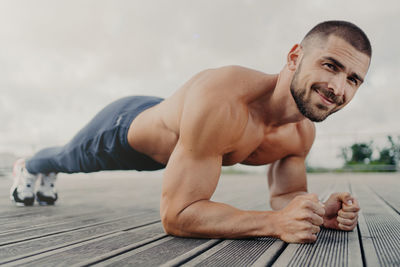 Portrait of shirtless young man exercising on wood