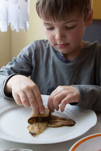 Boy folding beef kebab in eggplant slices in kitchen