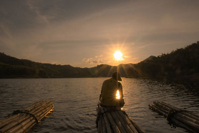 People on lake against sky during sunset