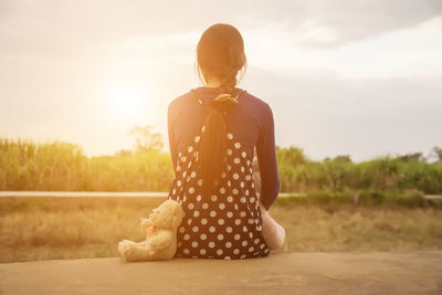 Rear view of woman standing on land against sky during sunset