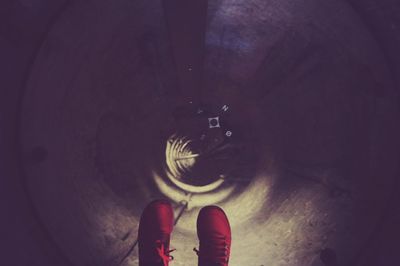 Low section of woman feet with red shoes hanging against manhole