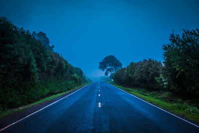 Empty road along trees and against blue sky