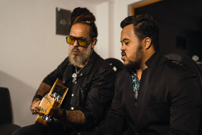 Adult bearded men in black clothes playing guitar and singing song in light studio