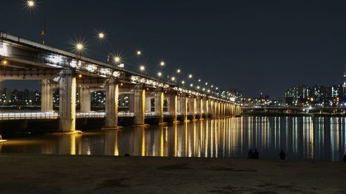 Illuminated bridge over river against sky at night