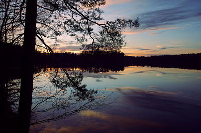 Silhouette trees by lake against sky at sunset