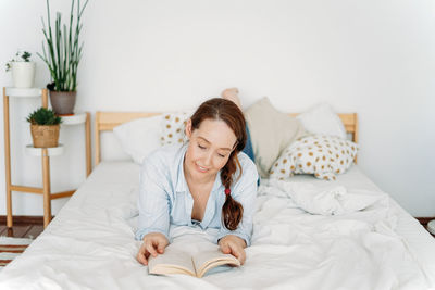 Woman reading book while lying down on bed