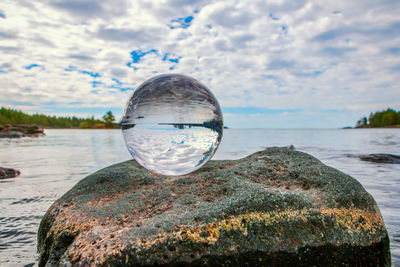 Close-up of crystal ball on rock by sea against sky