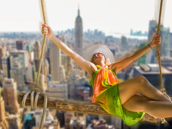 Digital composite image of woman swinging against manhattan