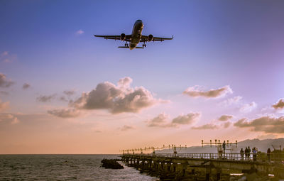 Airplane flying over sea against sky during sunset