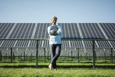 Mature man with laptop standing barefoot on meadow, solar plant