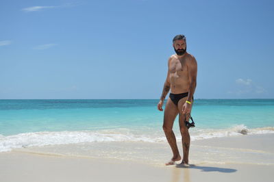 Full length of shirtless man standing at beach against sky