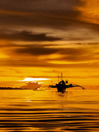 Silhouette boats in sea against dramatic sky during sunset