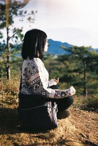 Side view of woman sitting in lotus position on landscape