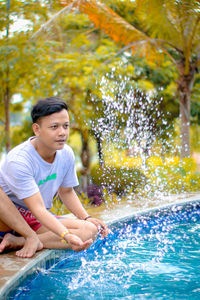 Man splashing water while sitting by poolside