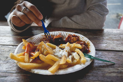Midsection of woman eating french fries with meat in plate on wooden table
