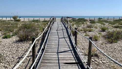 Walkway leading towards sea against sky