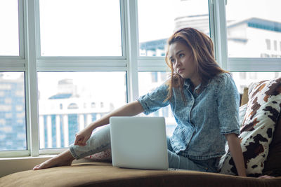 Young woman using phone while sitting on window