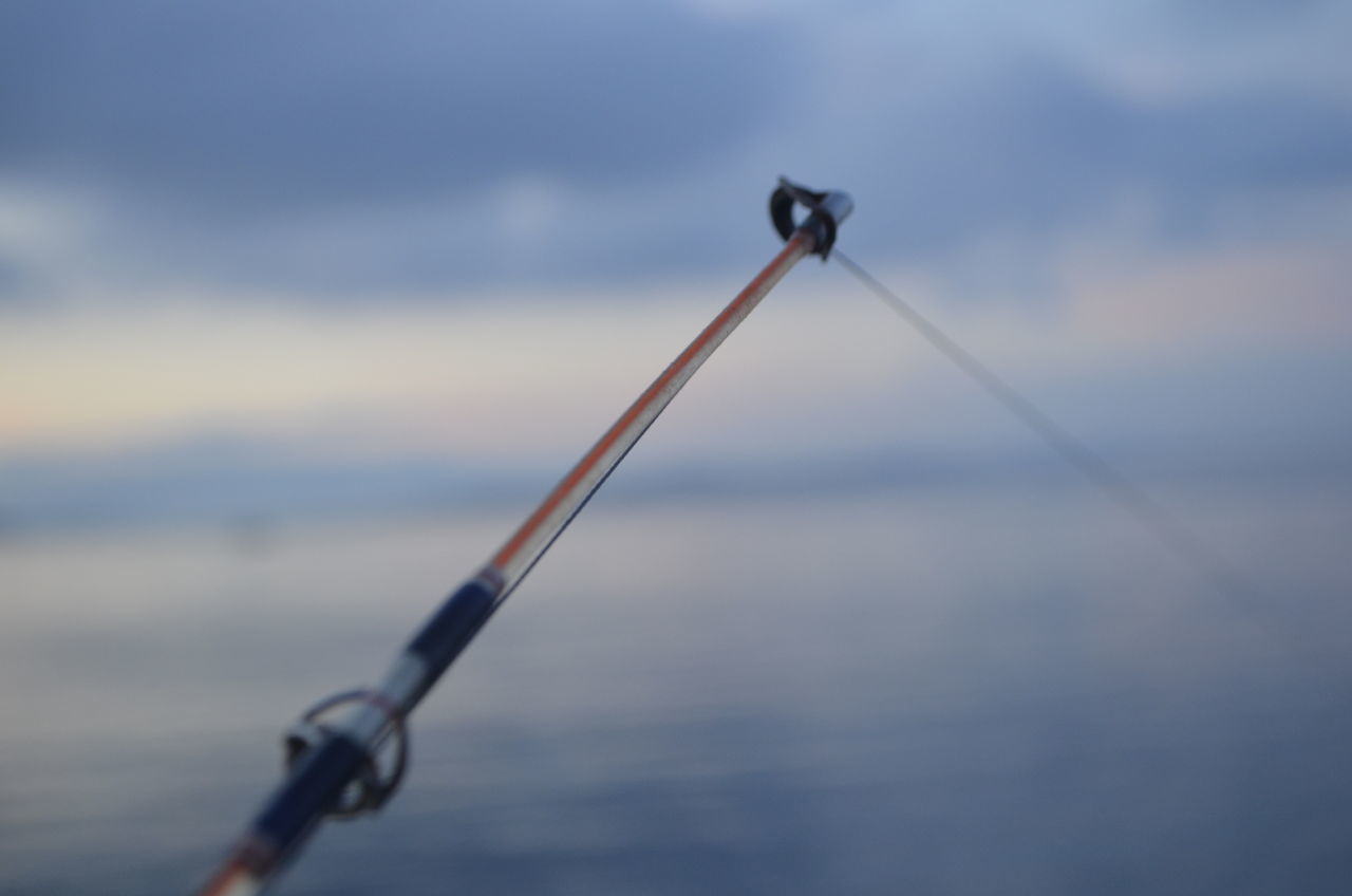 CLOSE-UP OF FISHING ROD BY SEA