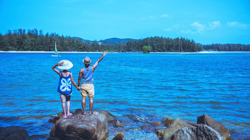 Rear view of couple standing on rock against sea and sky