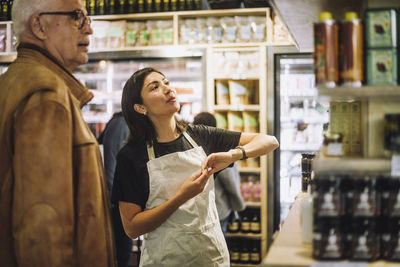 Saleswoman talking with senior male customer at delicatessen