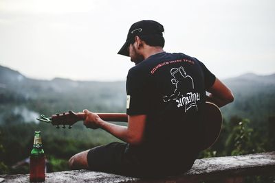 Young man sitting in bottle by mountains against sky