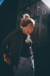 Beautiful young woman standing against wall at night