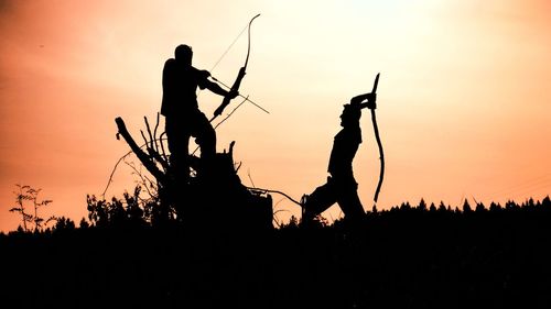 Silhouette men fighting on field against orange sky