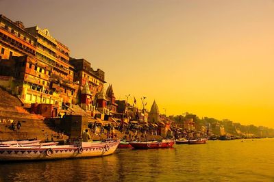 Boats moored on ganges river by temples against clear sky during sunset