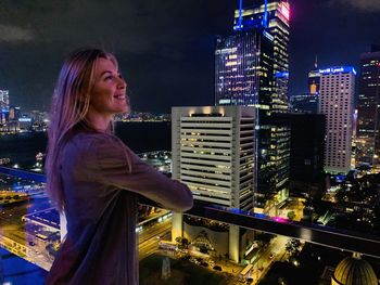 Side view of woman against illuminated buildings in city at night