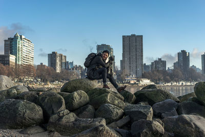 Full length of man sitting on rocks against blue sky