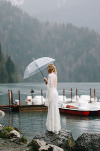 Beautiful young woman bride in a boho dress and with an umbrella stands in the rain in nature
