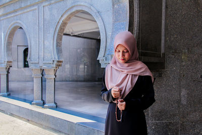 Portrait of young woman standing against wall