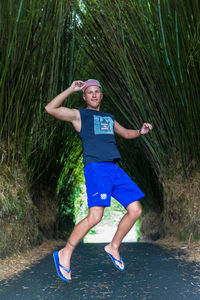 Portrait of young man in mid-air over road amidst bamboo trees