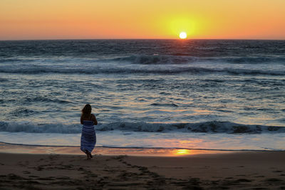 Woman standing on beach against sky during sunset