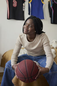Female teenager holding basketball while day dreaming in bedroom at home
