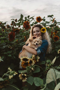 Woman carrying dog while standing amidst sunflowers