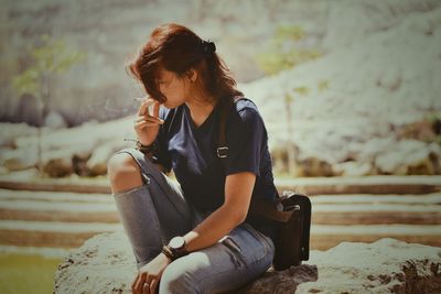 Young woman smoking cigarette while sitting outdoors