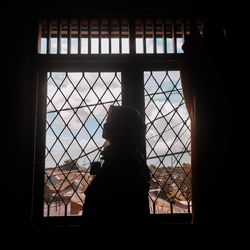 Silhouette woman looking through window in building