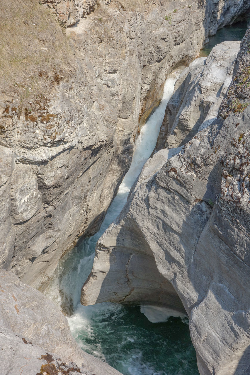 rock, water, beauty in nature, nature, rock formation, geology, cliff, scenics - nature, no people, land, cave, terrain, non-urban scene, day, high angle view, environment, wadi, sea, tranquility, landscape, outdoors, coast, physical geography, mountain, travel destinations, formation, tranquil scene, idyllic, travel, eroded, extreme terrain, sunlight