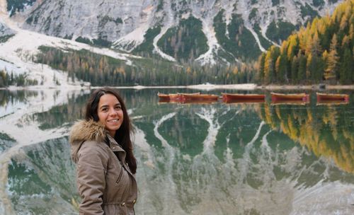 Portrait of smiling young woman standing against lake during winter