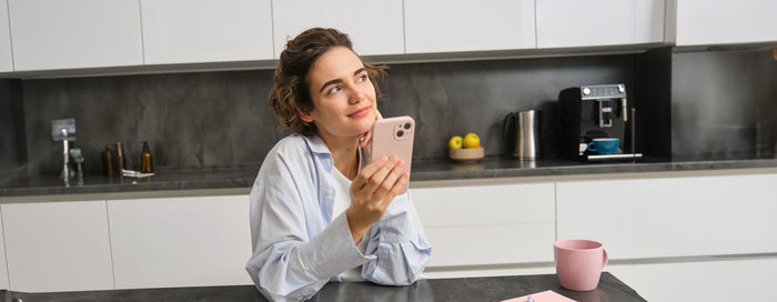 Young woman using mobile phone while standing in kitchen