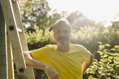 Smiling man leaning on ladder during sunny day