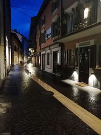 Wet street amidst buildings in city at night