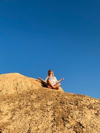 Low angle view of woman meditating on rock formation against clear sky